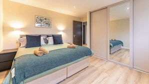 Ein Schlafzimmer mit Bett, Nachttischen, einem Spiegel und einer Tür zu einem anderen Raum.