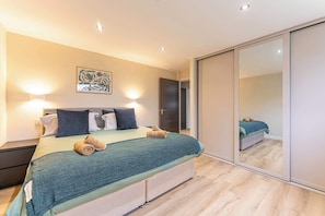 Ein Schlafzimmer mit Bett, Nachttischen, einem Spiegel und einer Tür zu einem anderen Raum.