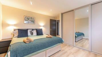 Un dormitorio moderno con cama, lámparas de noche, un espejo grande y una puerta que da a otra habitación.