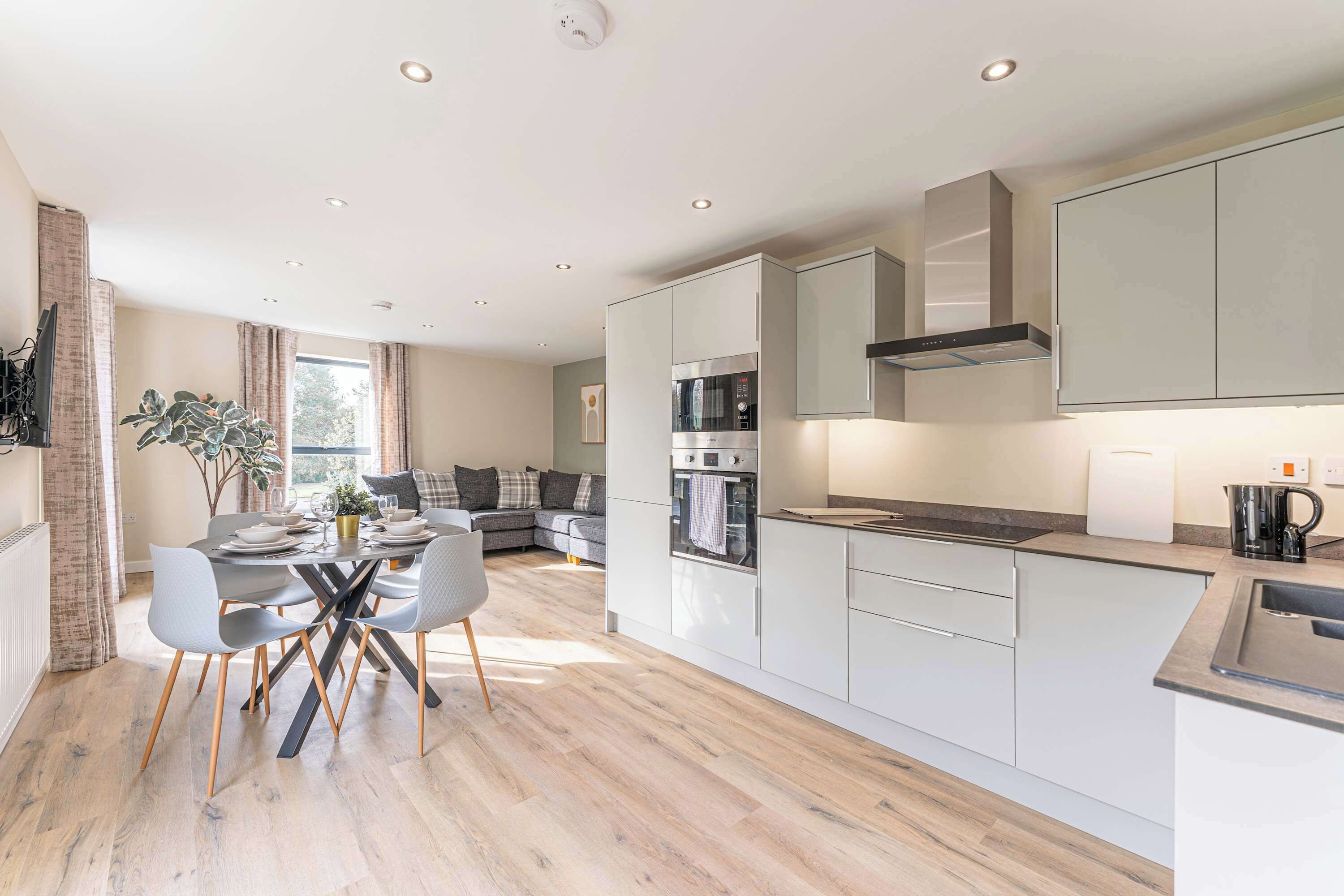 A modern kitchen with white cabinets, a built-in oven, and a dining area with a table and chairs.