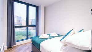 Een hotelkamer met een groot raam, een bed met witte lakens en uitzicht op gebouwen.
