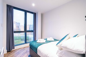 Ein Hotelzimmer mit großem Fenster, einem Bett mit weißer Bettwäsche und Blick auf Gebäude.