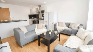 Una sala de estar moderna con un sofá gris, una mesa de centro y una cocina al fondo.
