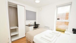 Un dormitorio con cama, escritorio, silla, armario y ventana.