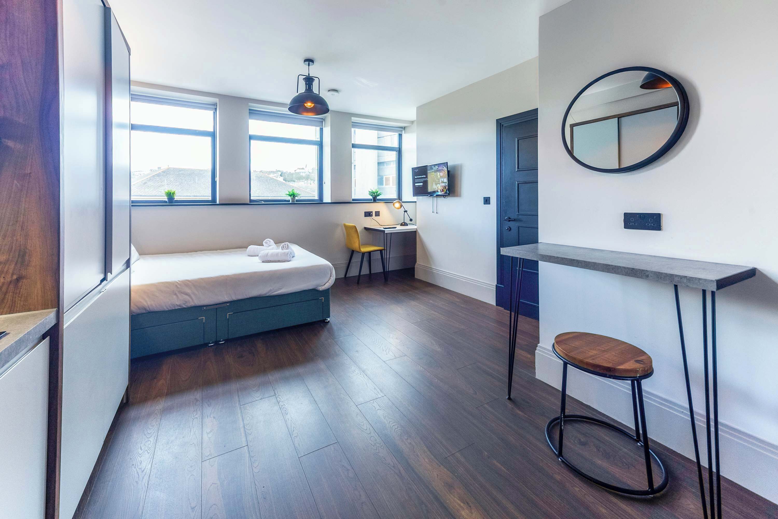 Een moderne kamer met een bed, bureau, stoel en een ronde spiegel aan de muur.