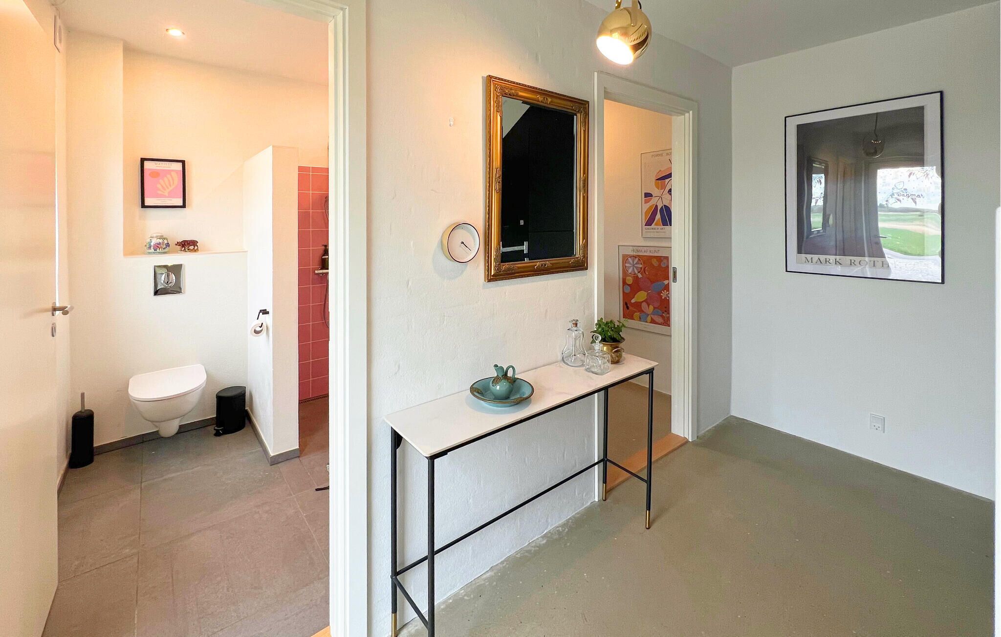 A hallway with a white toilet, a small table with a plant, a mirror, and a framed picture on the wall.