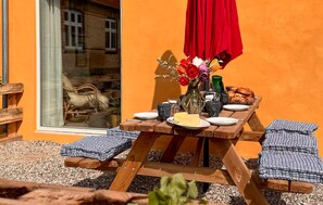 Ein Holztisch für ein Picknick, mit einem roten Sonnenschirm, einer Blumenvase und Tellern mit Essen.