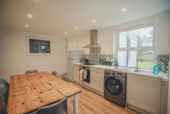 Una cocina moderna con una mesa de comedor de madera para seis personas, horno empotrado, lavadora y un gran ventanal con vistas al exterior.