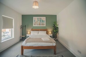 Un dormitorio con cama, lámparas de noche, una ventana y un cuadro en la pared.