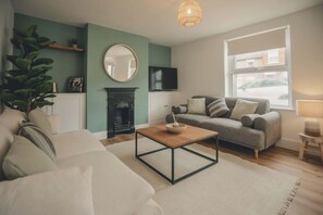 Una sala de estar con sofá, mesa de centro, chimenea, televisor y ventana con vista a la calle.