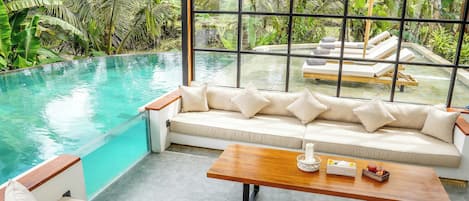 Ein Poolbereich mit Sofa und Tisch, umgeben von üppiger Vegetation und einem klaren Pool.