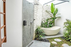 Een moderne badkamer met een vrijstaand bad, een douche en een stenen muur.