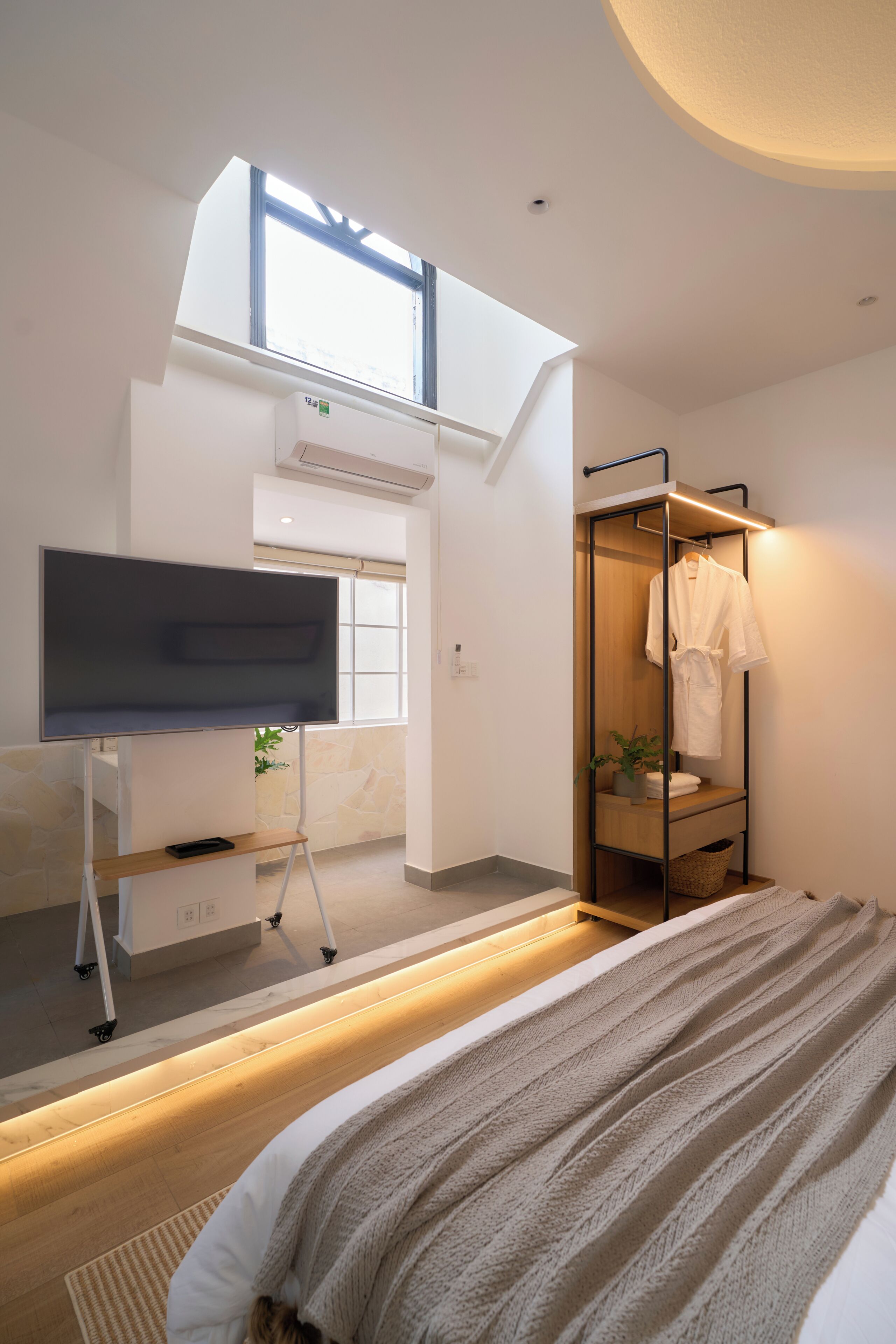 A modern bedroom with a bed, a TV on a stand, a wardrobe, and a skylight.