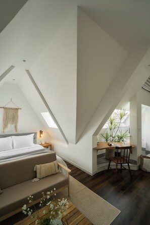A modern loft bedroom with a sloped ceiling, a bed, a seating area, and a workspace with a desk and chair. - Hanachi Stay Thao Dien (Ho Chi Minh City)