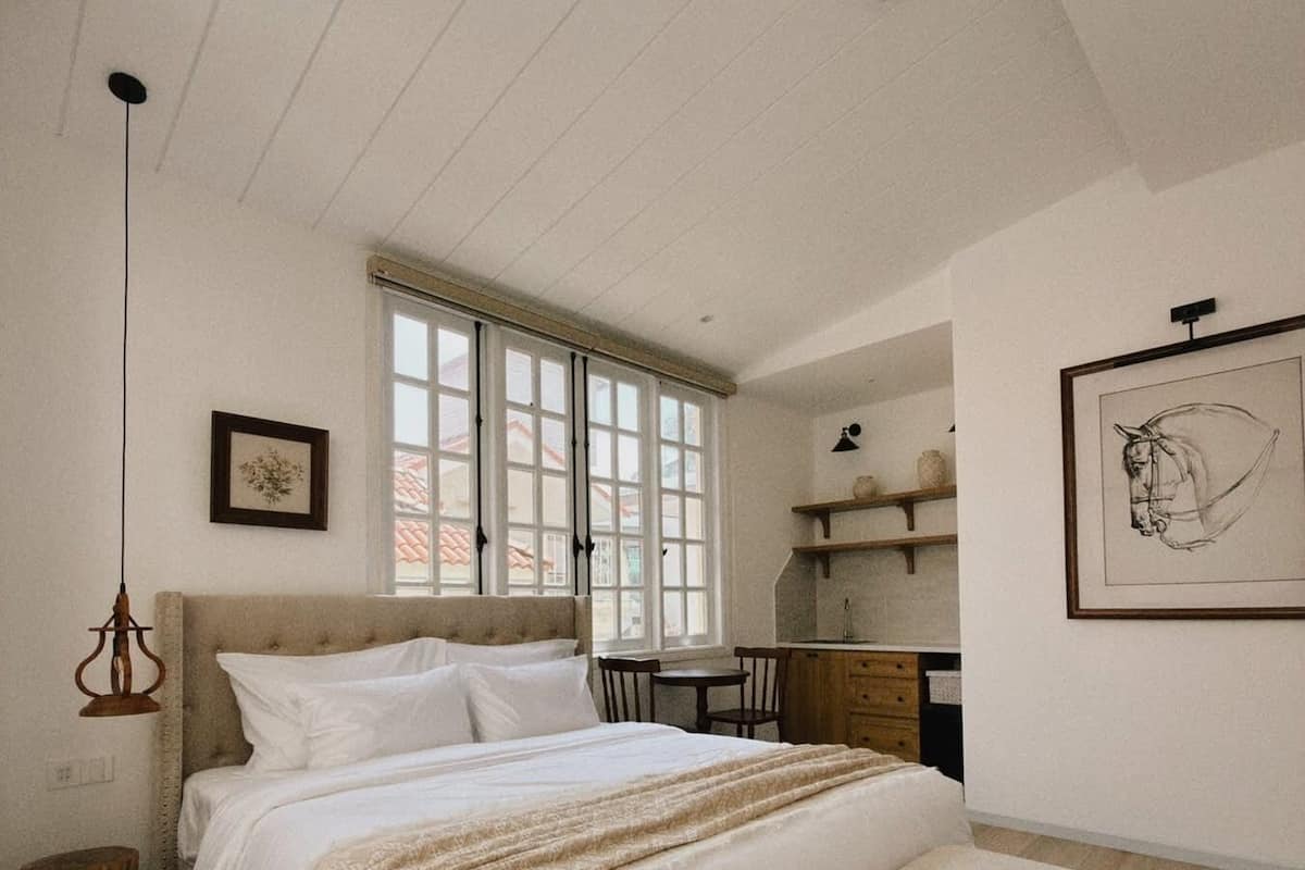 Un dormitorio con una cama grande, un banco, un escritorio y una ventana.