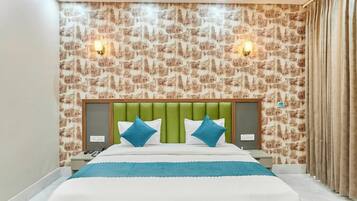 Una habitación de hotel con cama, cabecera verde, dos apliques de pared y papel tapiz estampado.