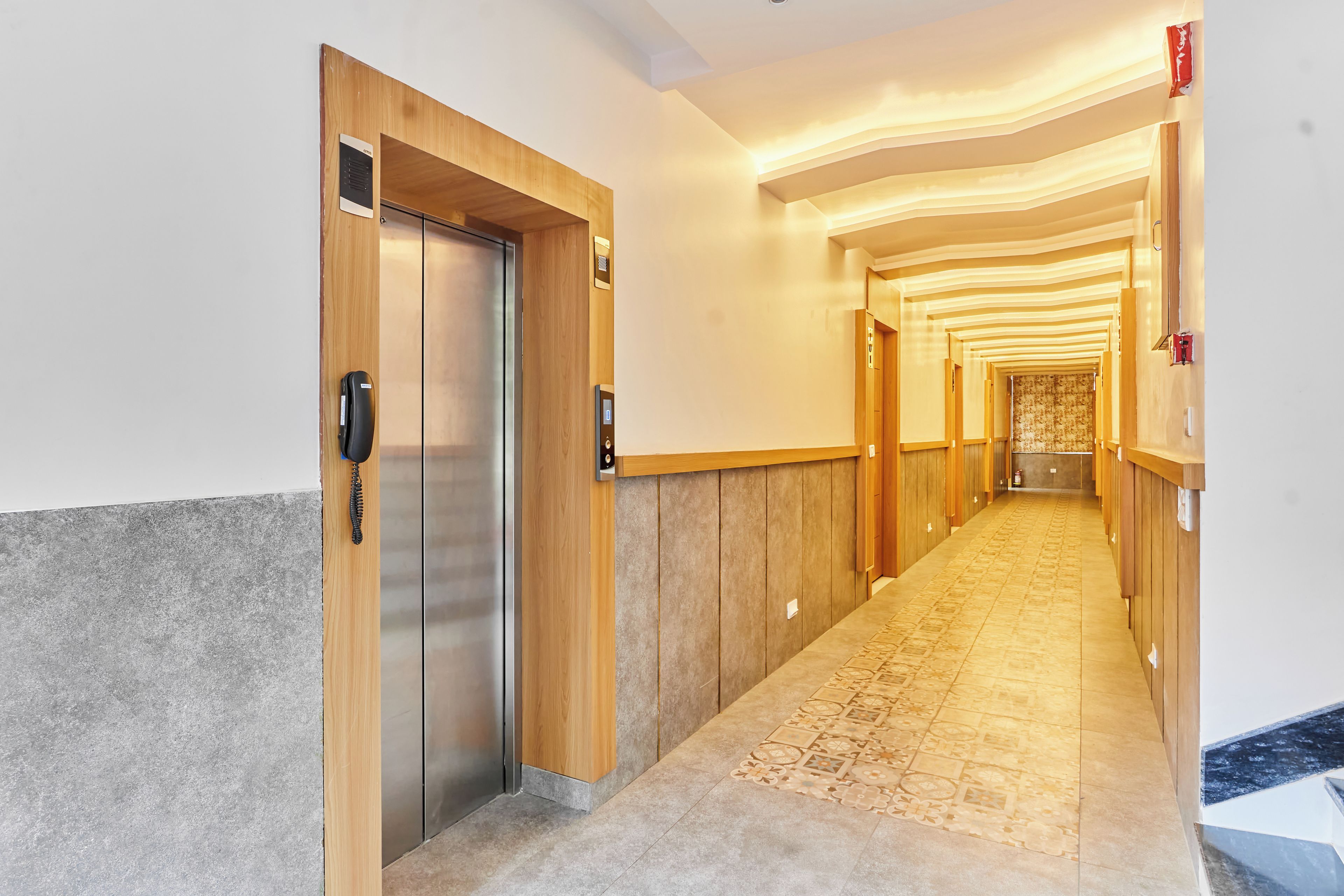 Un couloir d’hôtel avec des portes en bois, un sol à motifs et un luminaire moderne.
