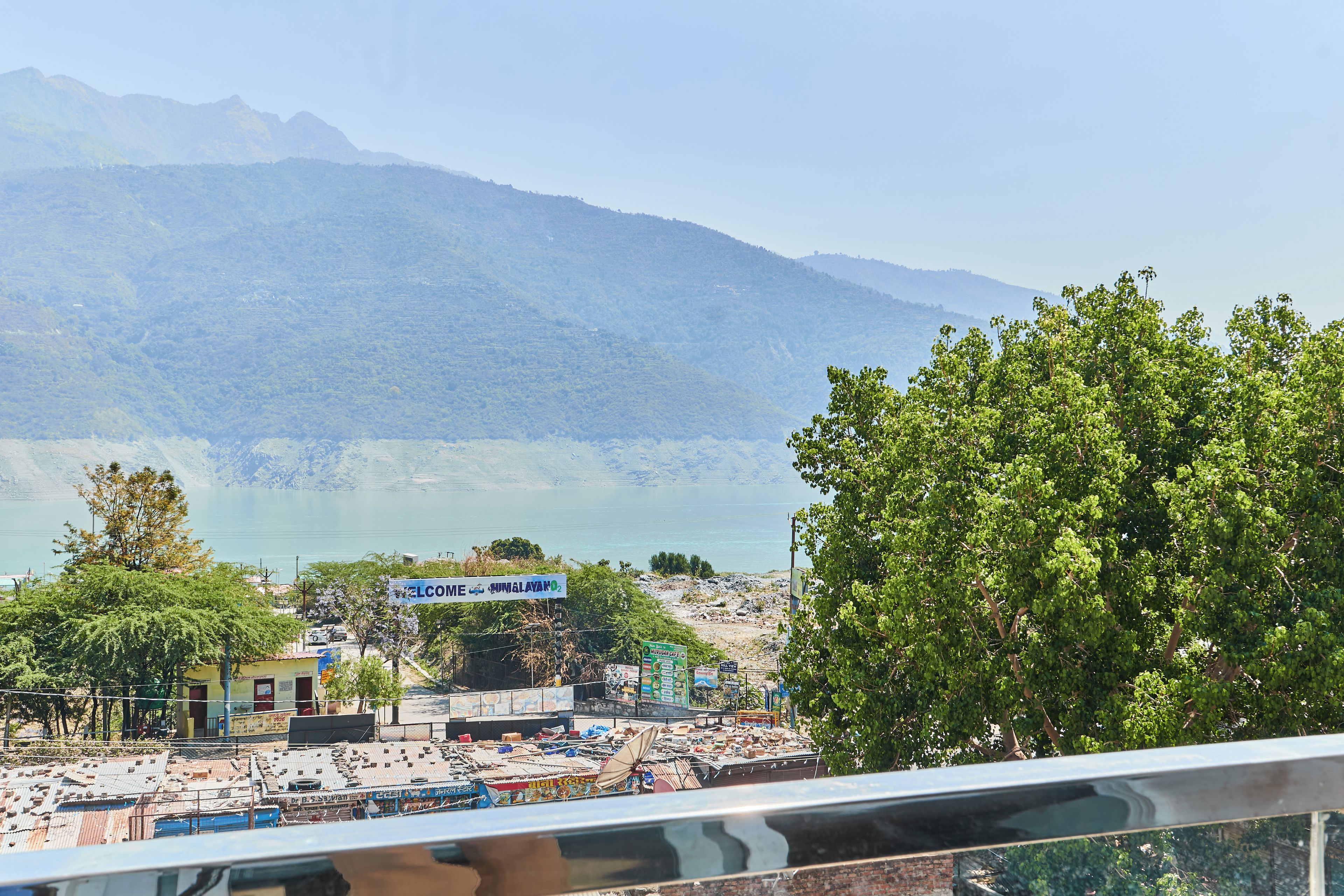 A coastal area with a view of the sea and mountains in the background. There are buildings with signage, including one that says 'WELCOME HIMALAYAN O2'.