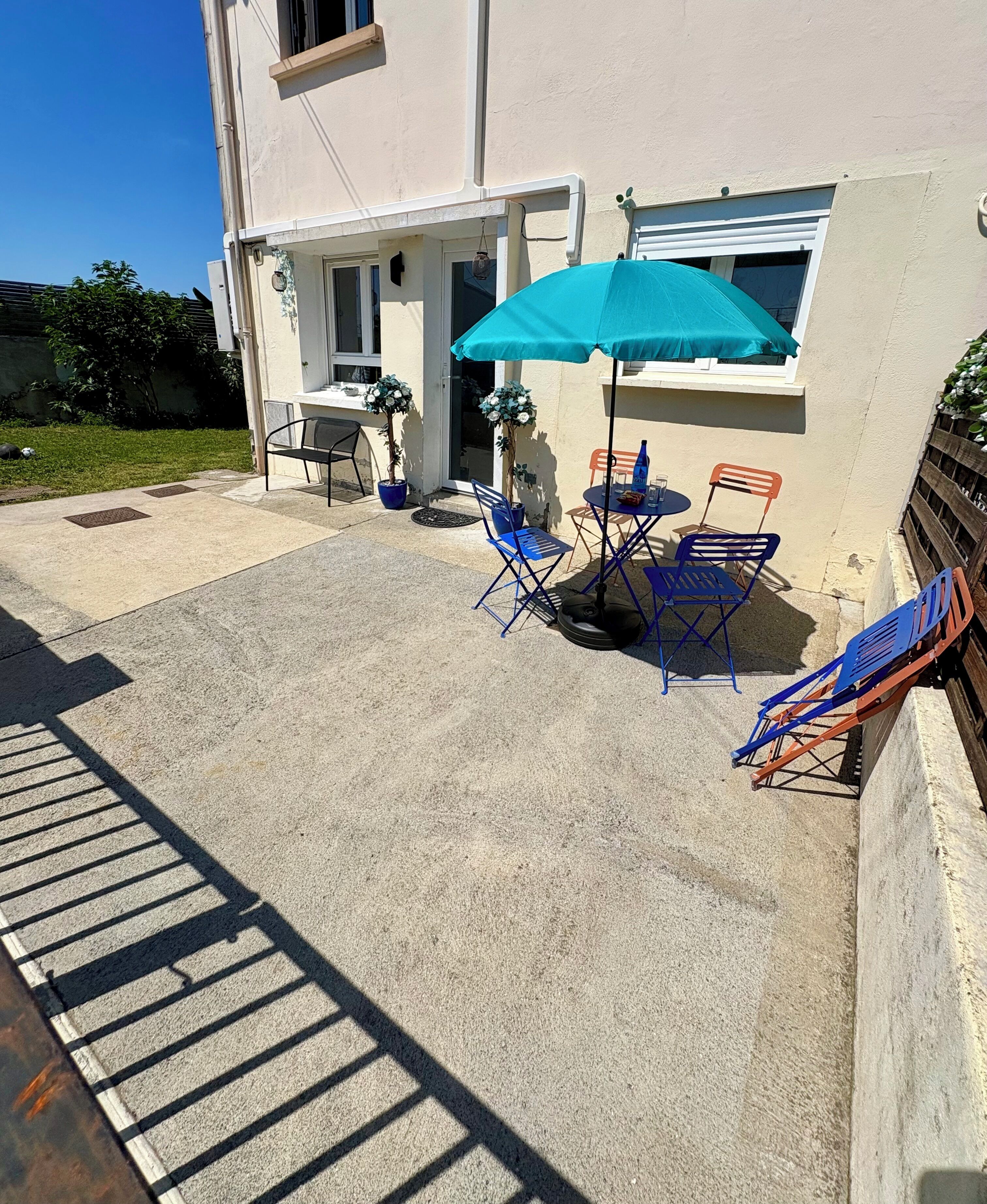 Eine Terrasse mit Tisch, Stühlen, einem blauen Sonnenschirm und Topfpflanzen.