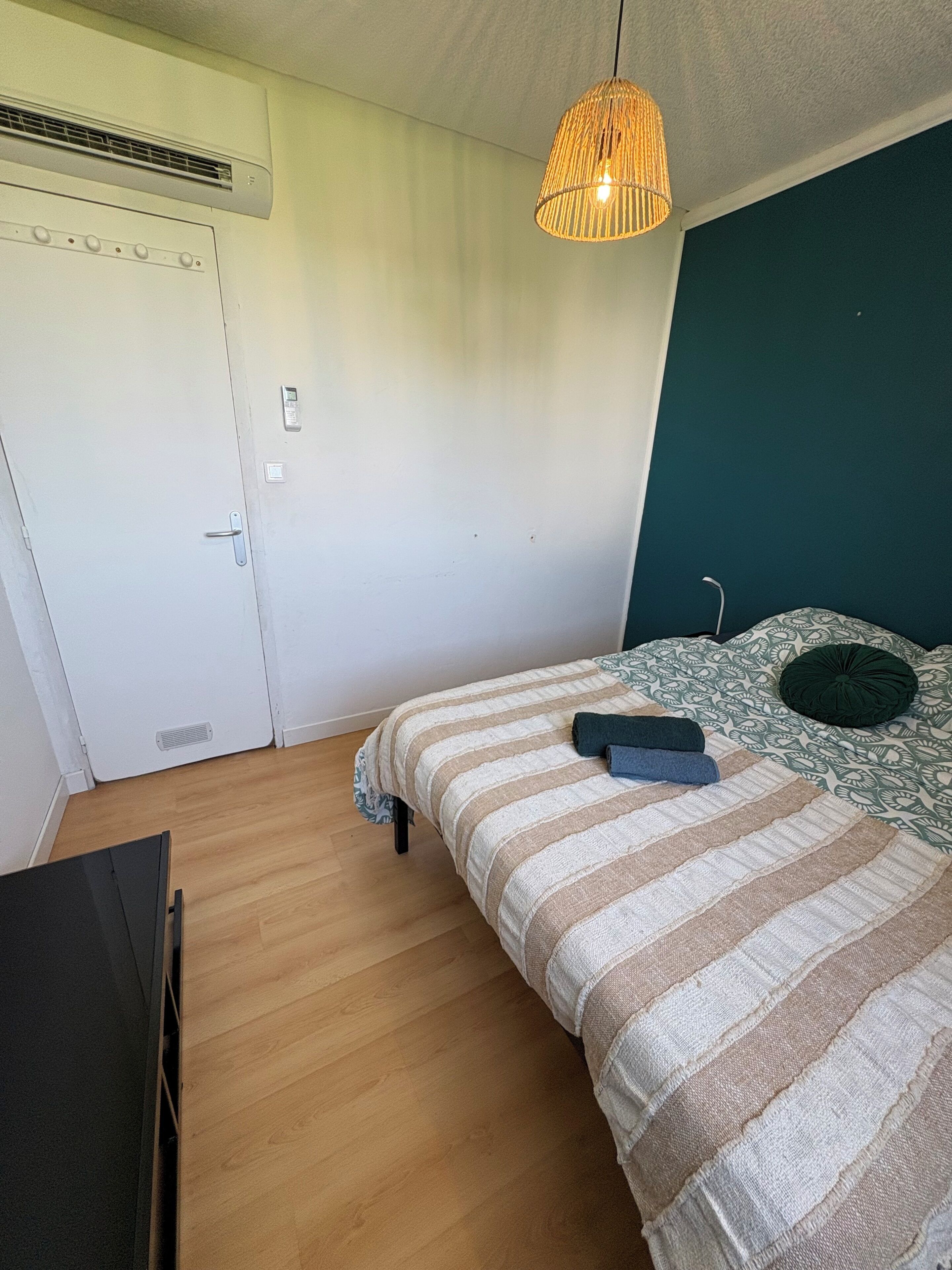 A bedroom with a bed, a hanging light fixture, a white door, and a wooden floor.