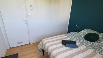 A bedroom with a bed, a hanging light fixture, a white door, and a wooden floor.