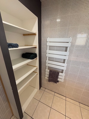 Une salle de bain avec un mur de douche recouvert de carreaux, un porte-serviettes blanc et une étagère intégrée.