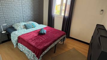 Een slaapkamer met een metselwerkmuur, een bed met beddengoed met een patroon, een rode deken, een hangende oranje lamp en een raam met gordijnen.