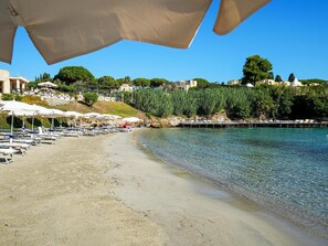 Une plage avec des parasols, des chaises longues et une vue dégagée sur l’eau.