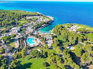 An aerial view of a coastal resort with a swimming pool, beachfront villas, and lush greenery. - Hotiday Torre Santo Stefano Resort (Otranto)