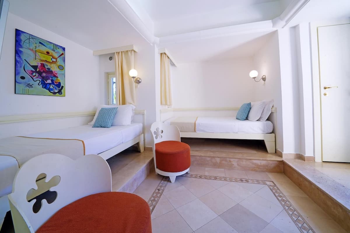 A hotel room with two beds, a small table, a chair, a colorful painting, and a window with curtains.