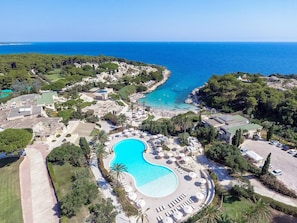 Une vue aérienne d’un complexe hôtelier doté d’une grande piscine, de villas en bord de mer et offrant une vue dégagée sur l’océan.