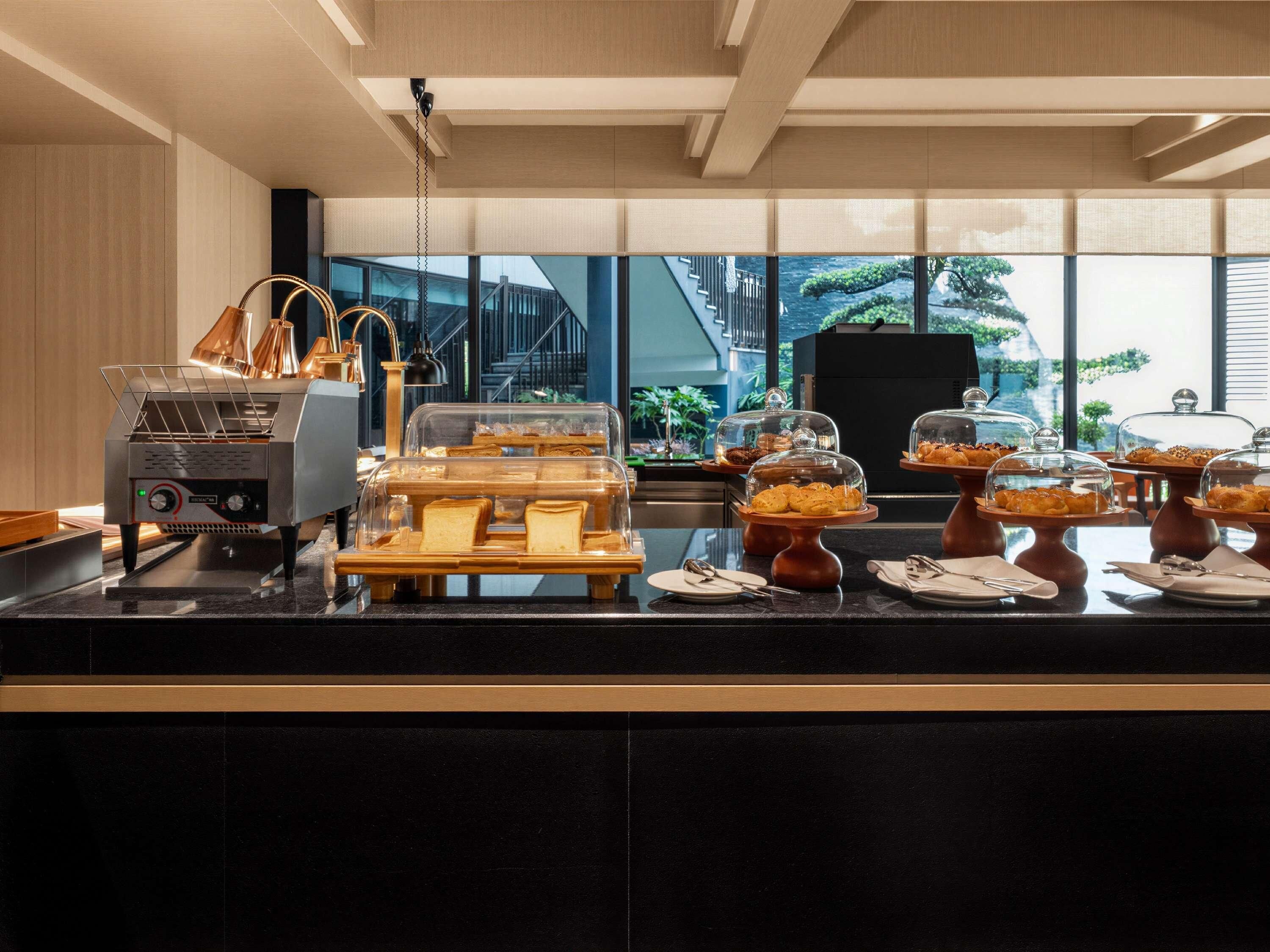 Un buffet proposant divers plats, une machine à café et une vue sur un bâtiment à l’extérieur.