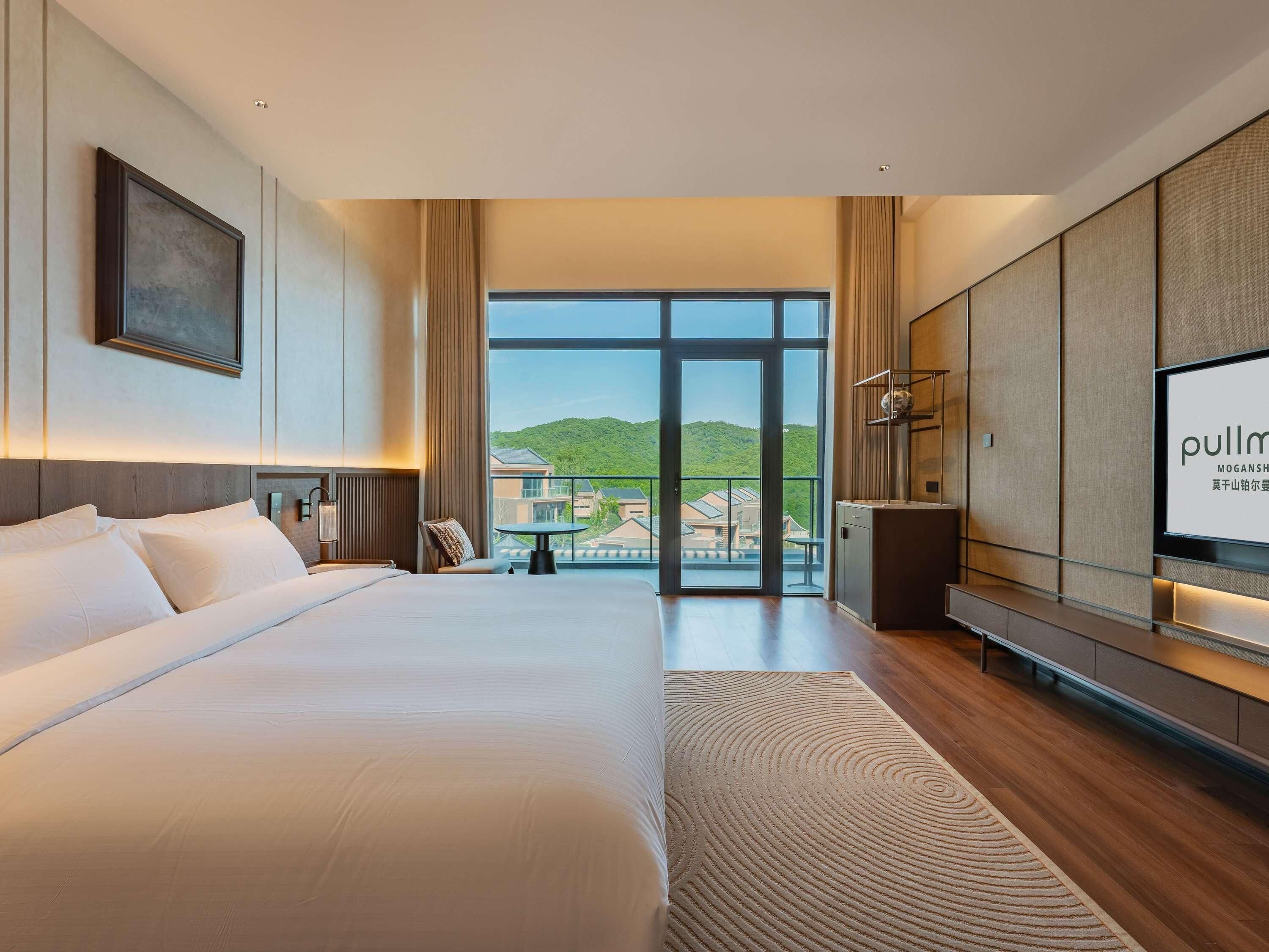 Habitación de hotel moderna con una cama grande, televisor y vista a un paisaje verde.