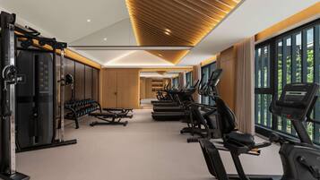 Une salle de sport moderne, dotée d’équipements d’exercice, de grandes fenêtres et d’un plafond en bois au design original.