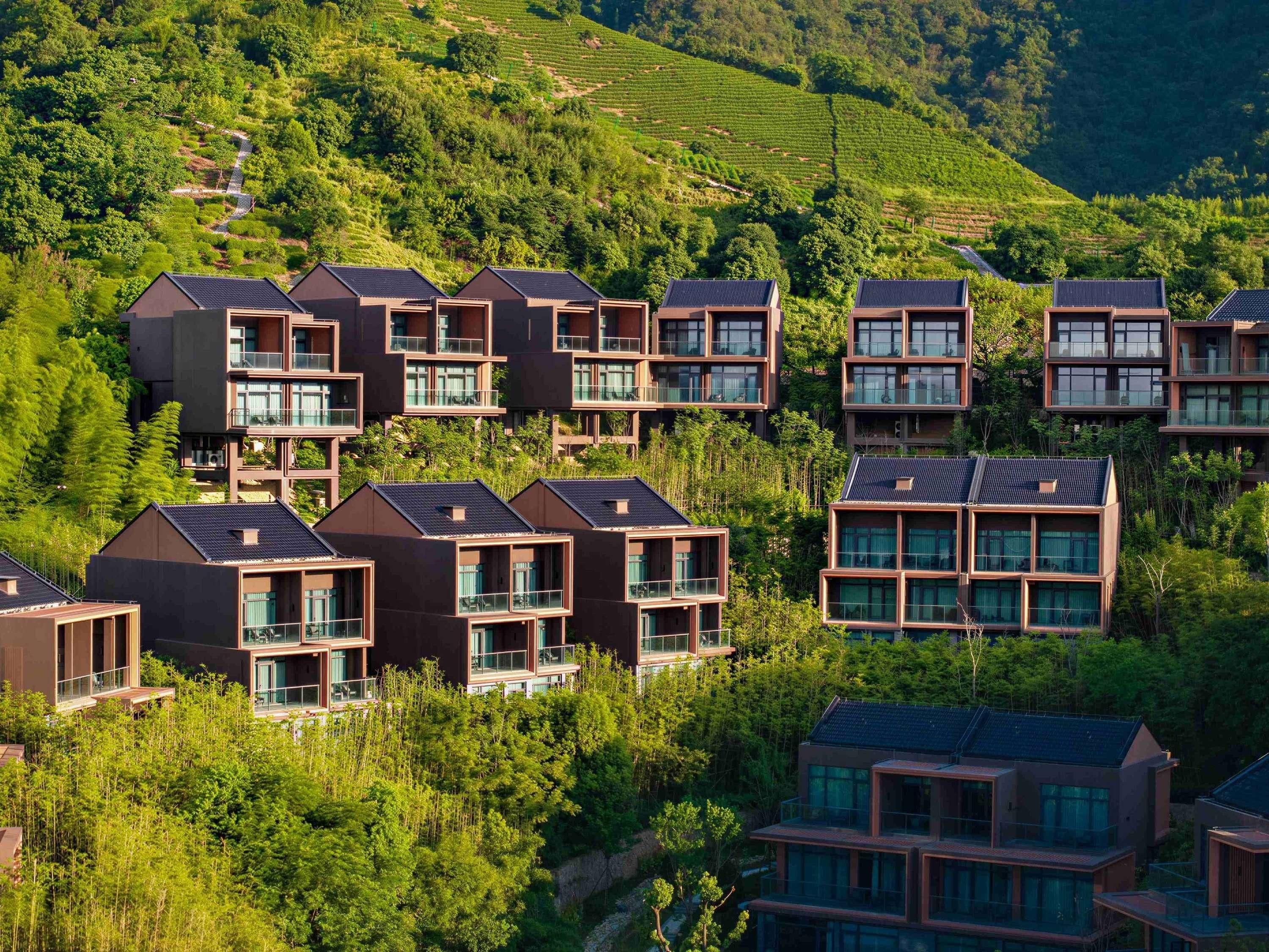 Un conjunto de modernos edificios residenciales de varios pisos con balcones, rodeado de exuberante vegetación y campos en terrazas.