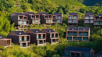 Un conjunto de modernos edificios residenciales de varios pisos con balcones, rodeado de exuberante vegetación y campos en terrazas.