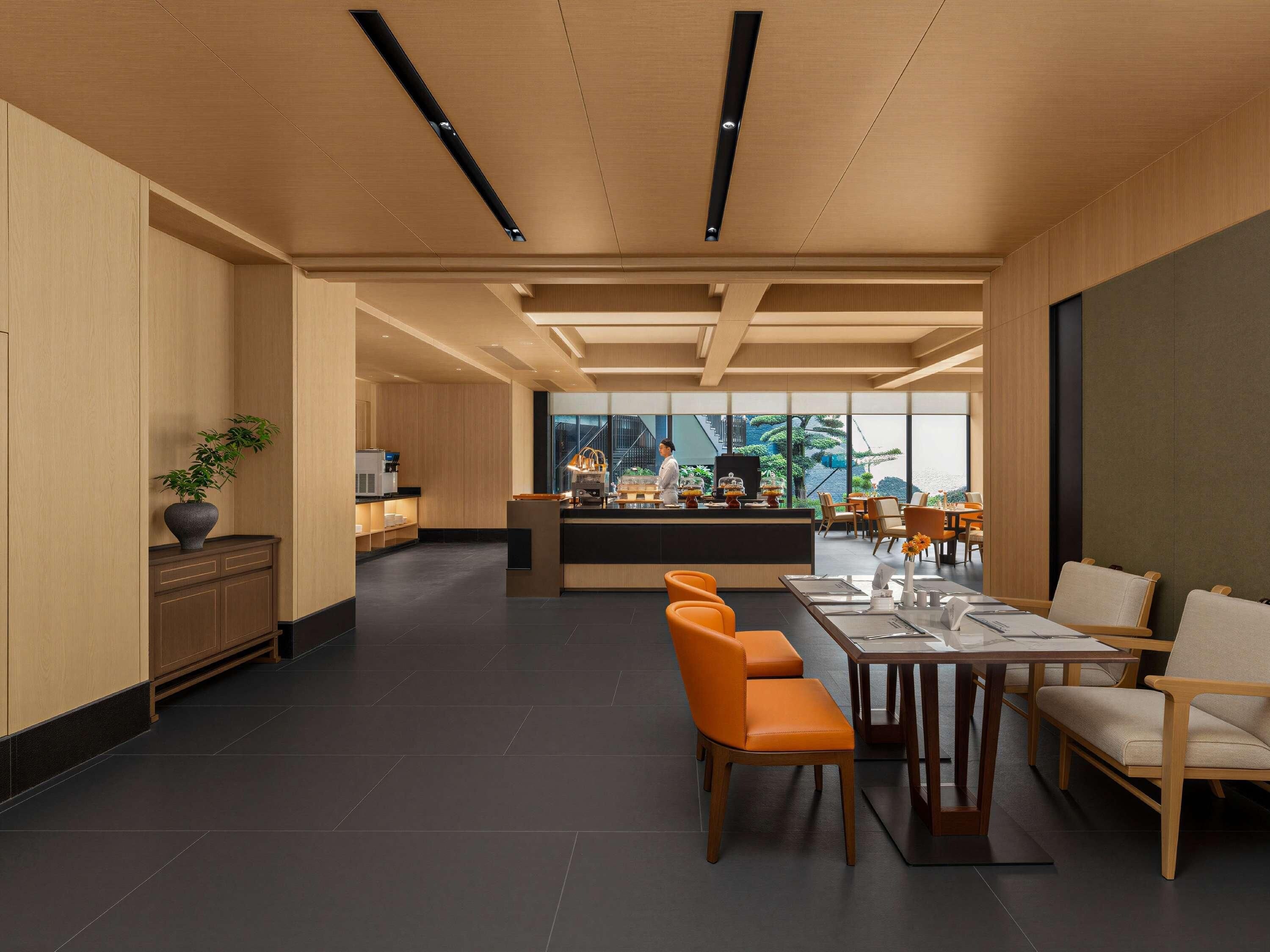 A modern hotel lobby with a central bar area, seating arrangements, and a view of the outdoors.