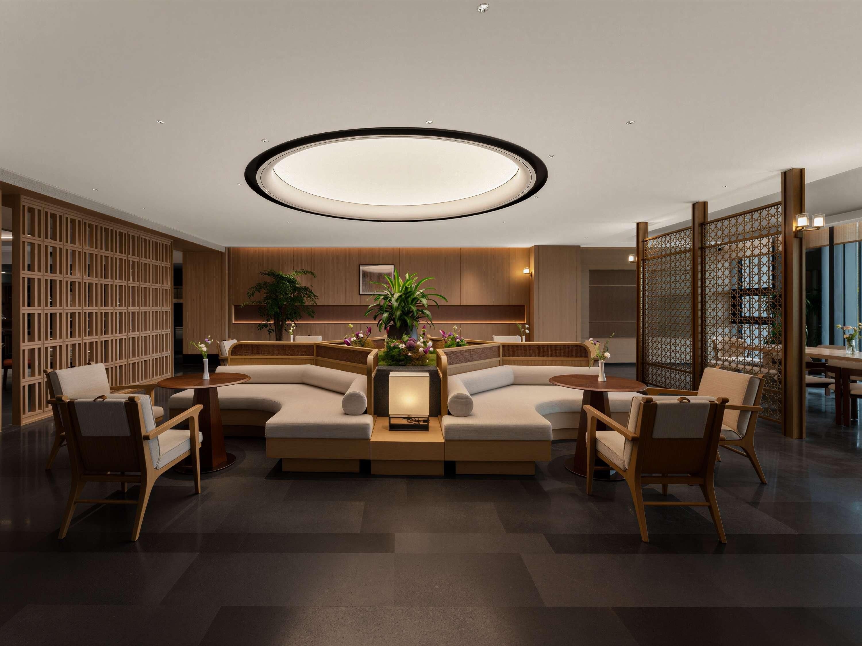 Un moderno hall de hotel con una zona de estar central, separadores de madera y una gran lámpara circular.