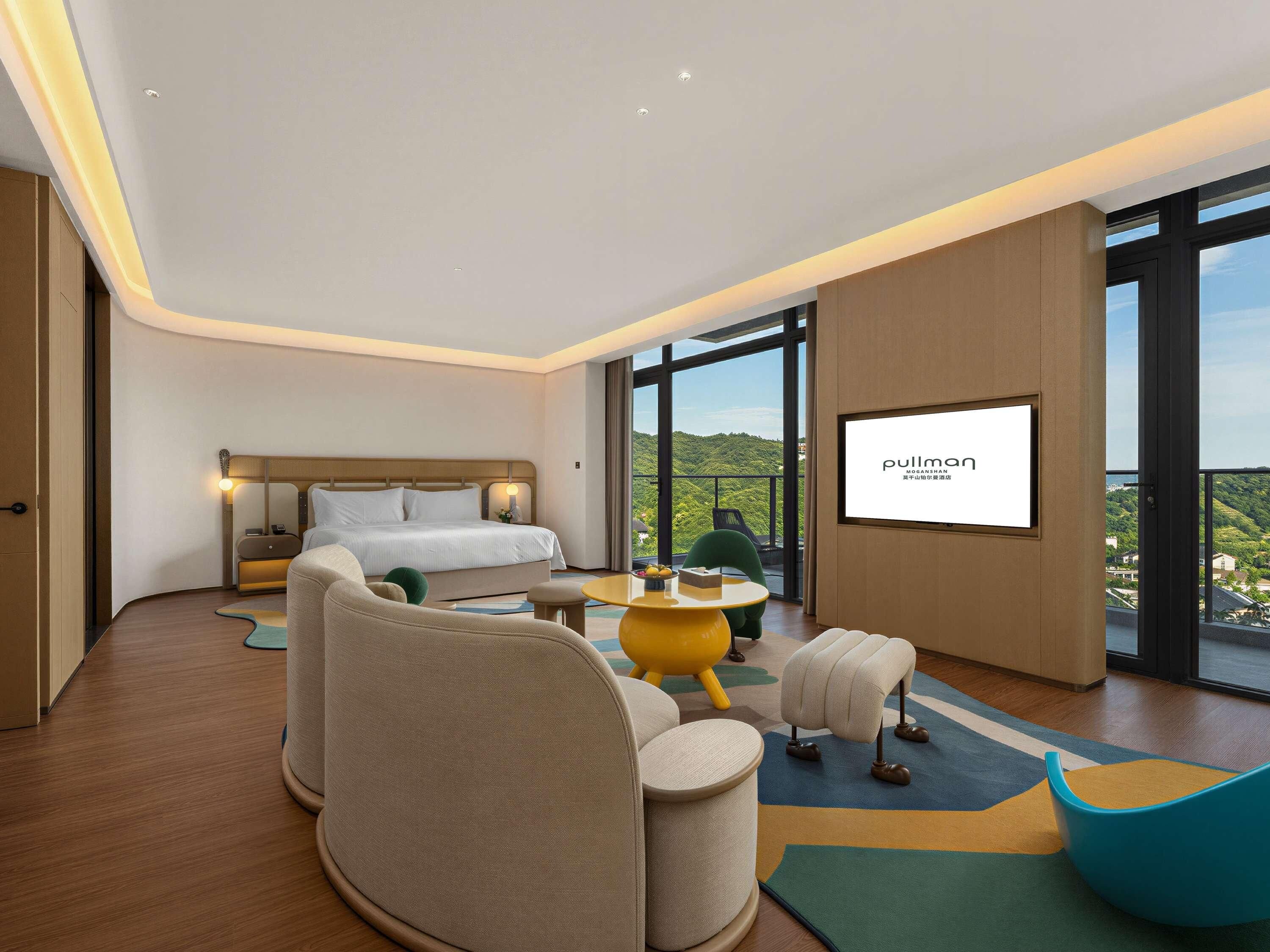 A hotel room with a bed, seating area, and a large window with a view.