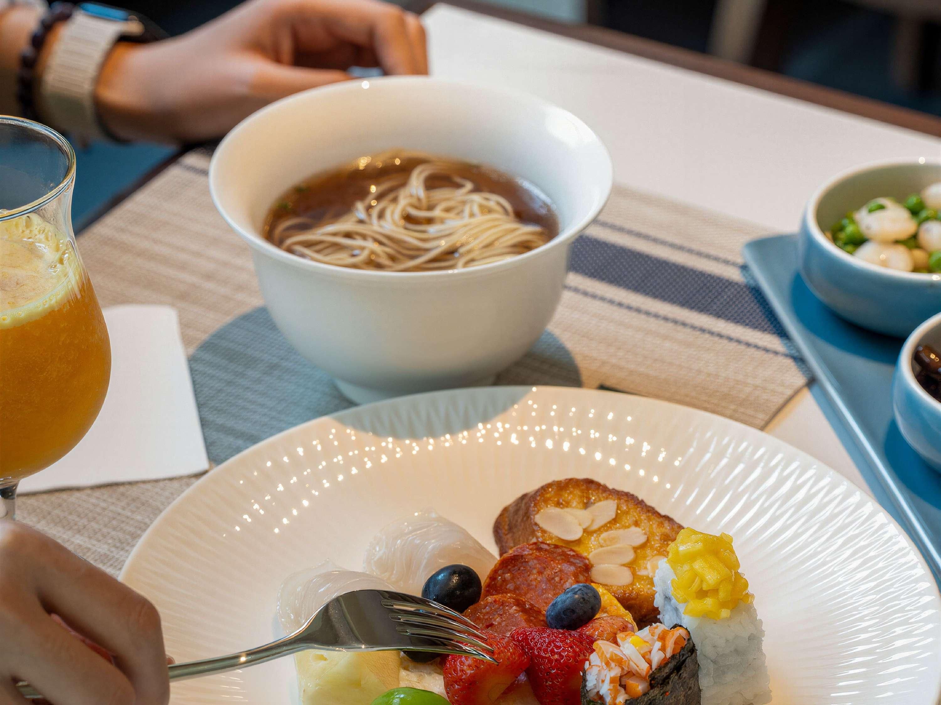 Une table à manger avec une assiette de nourriture, un bol de soupe et un verre de jus d’orange.