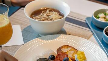 Une table à manger avec une assiette de nourriture, un bol de soupe et un verre de jus d’orange.