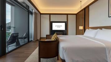 Habitación de hotel con cama, televisor, zona de estar y vistas a través de un ventanal.