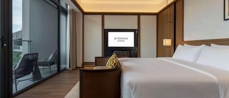 Habitación de hotel con cama, televisor, zona de estar y vistas a través de un ventanal.