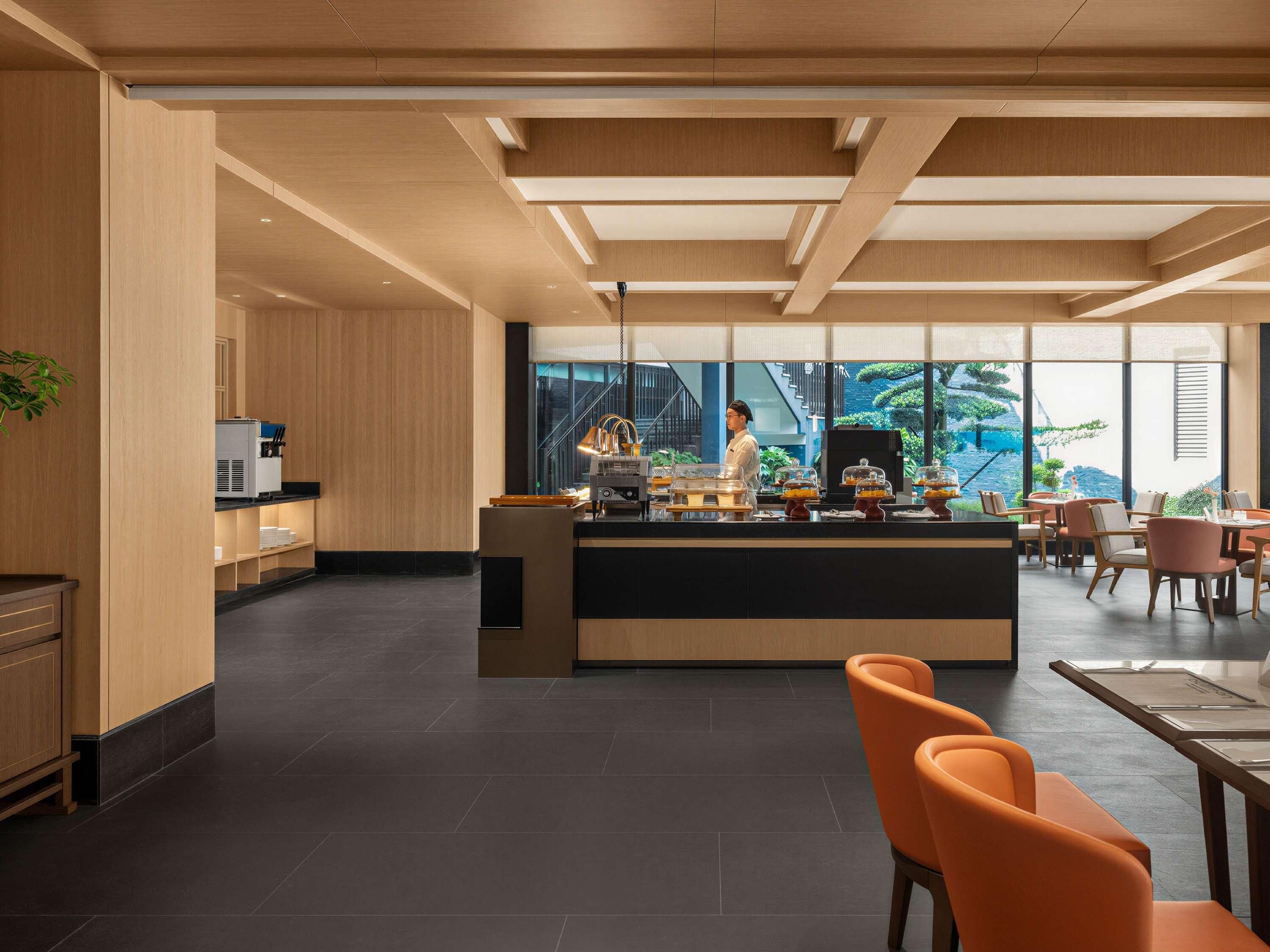 A modern hotel lobby with a central counter, seating area, and large windows offering a view of the outdoors.