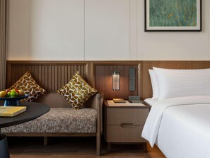 Ein Hotelzimmer mit Bett, Nachttisch, Lampe, Sessel und einem kleinen Tisch mit Obstschale.