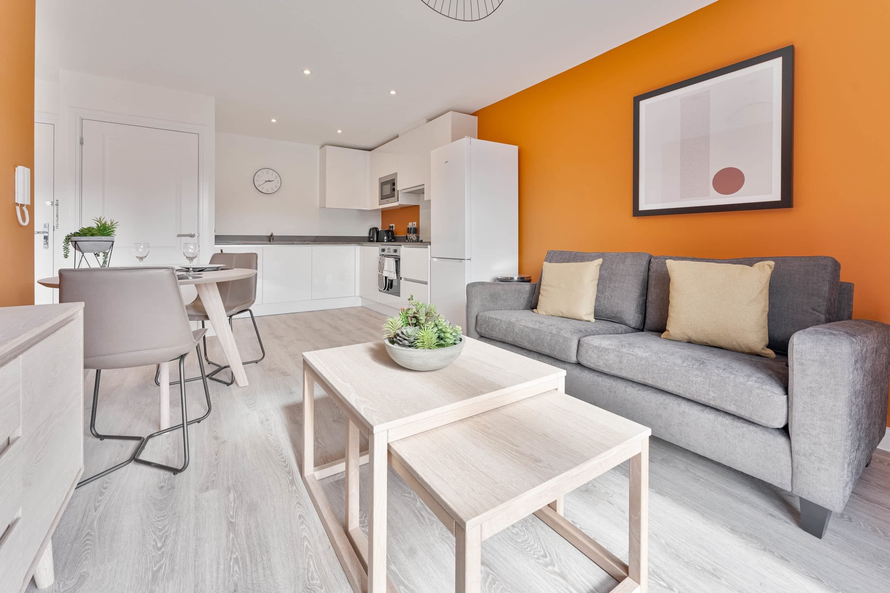 A modern living room with a grey sofa, a small wooden coffee table, and a dining area with a grey chair.
