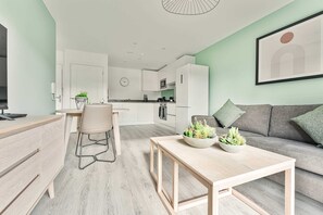 A modern living room with a sofa, a dining area with a table and chairs, a kitchen in the background, and a clock on the wall. - Stay Zeni, Hardwick House Derby Lovely 1 Bed Flat (Derby)