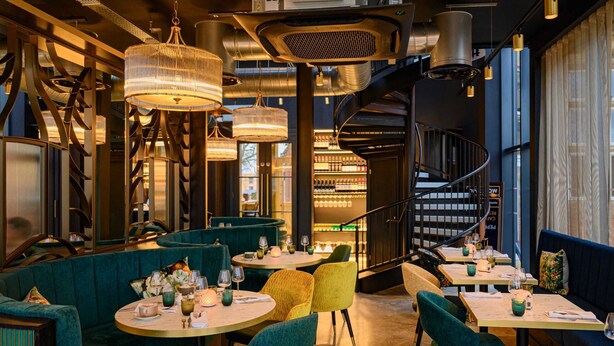 Un restaurant avec des tables rondes, des sièges rembourrés, des luminaires suspendus et un escalier en colimaçon.