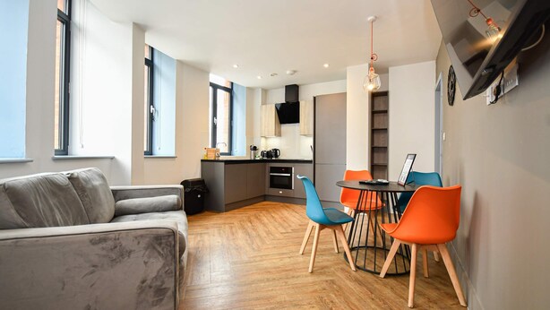 A modern living room with a sofa, a dining table with chairs, and a kitchen area in the background. - Spacious 2BED Central Manchester Flat w Security (Salford)