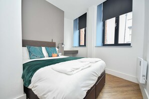 Ein Schlafzimmer mit einem Bett, einem Nachttisch, einem Fenster und einer Wandheizung.